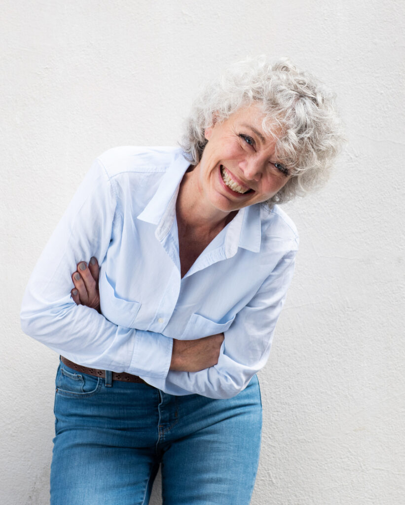Older woman laughing with dentures against gray wall